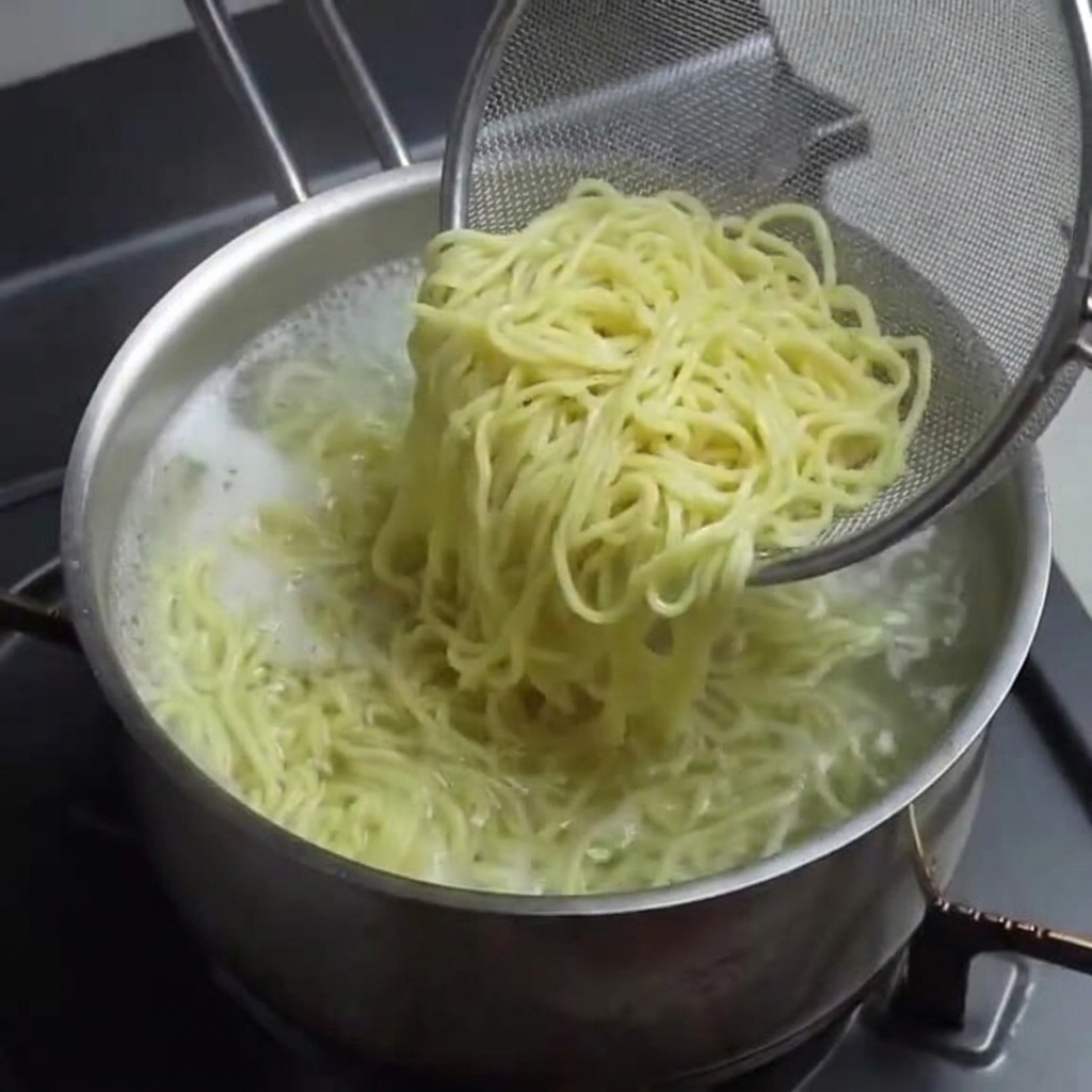 Cooked ramen noodles being lifted from a pot with a wire mesh strainer.