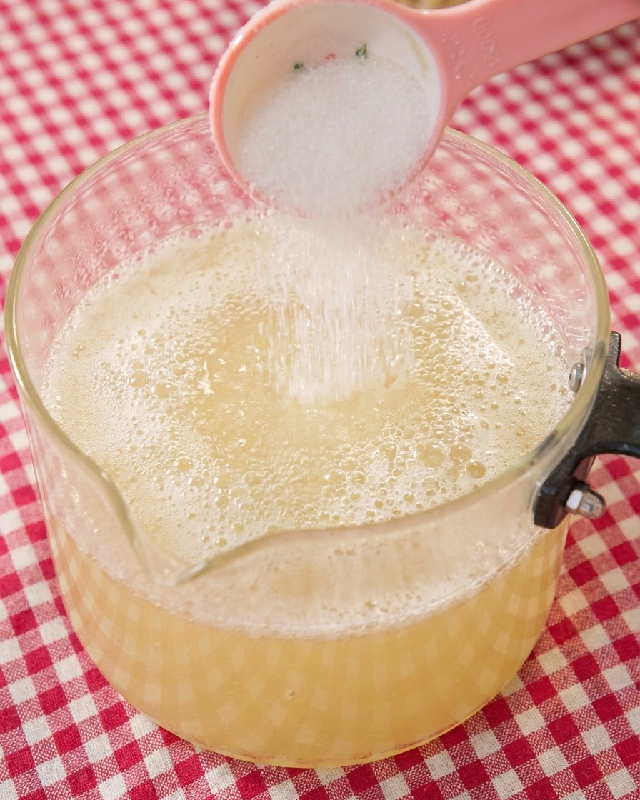 A spoonful of white sugar being added to the simmering ramen broth.