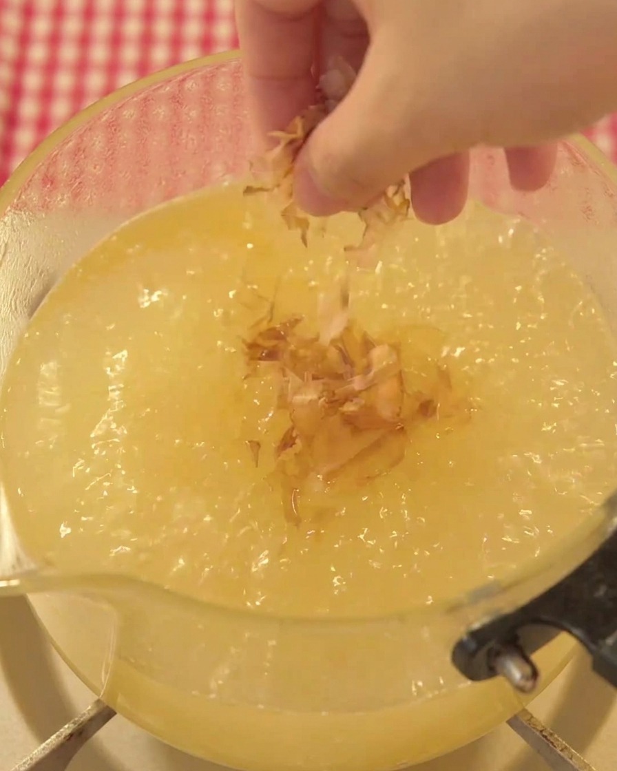 A pinch of dried bonito flakes being sprinkled into the boiling broth.