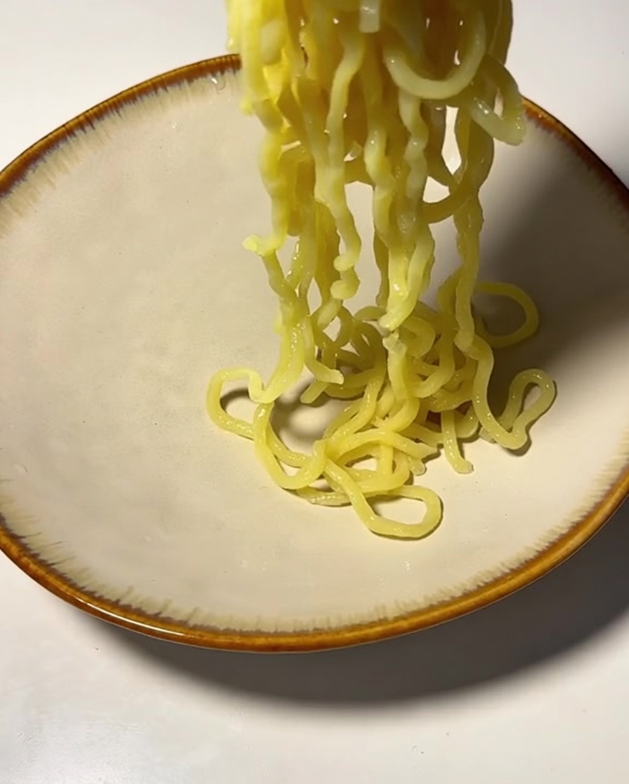 Cooked noodles being lifted into a ceramic bowl.