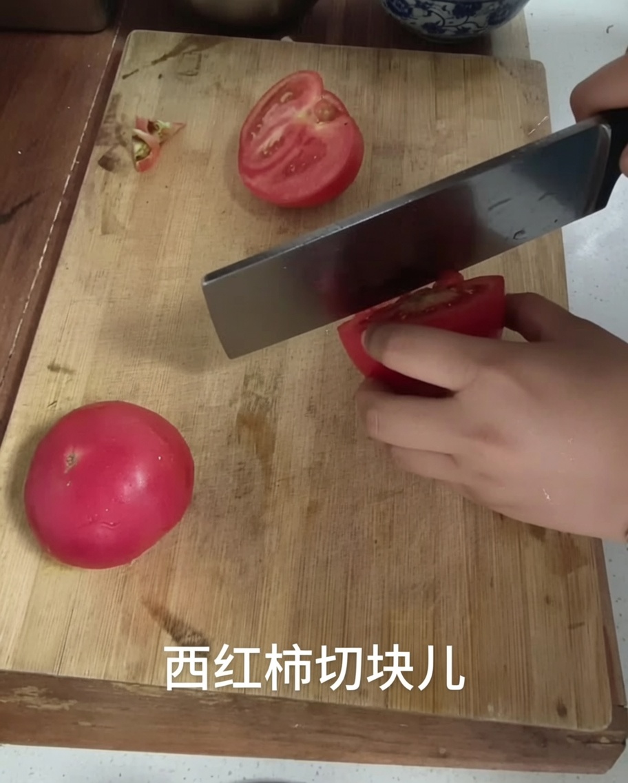 A kitchen knife cutting a tomato into chunks on a wooden cutting board.
