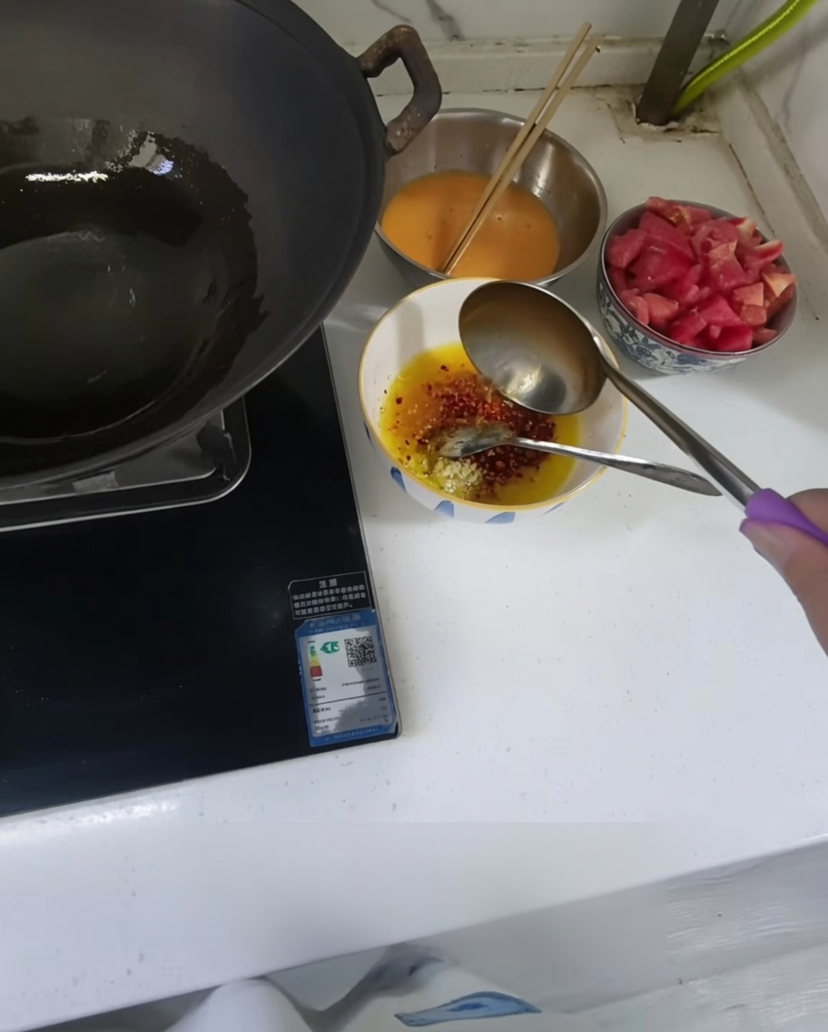 Hot oil being poured from a ladle into a small bowl containing minced garlic and chili powder.