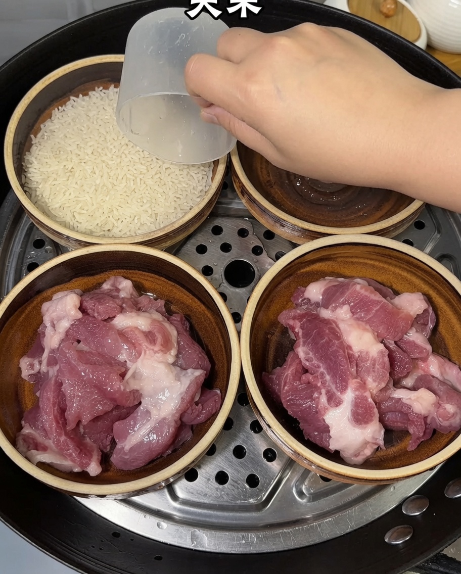 A hand using a measuring cup to add raw rice into bowls already containing pork slices.