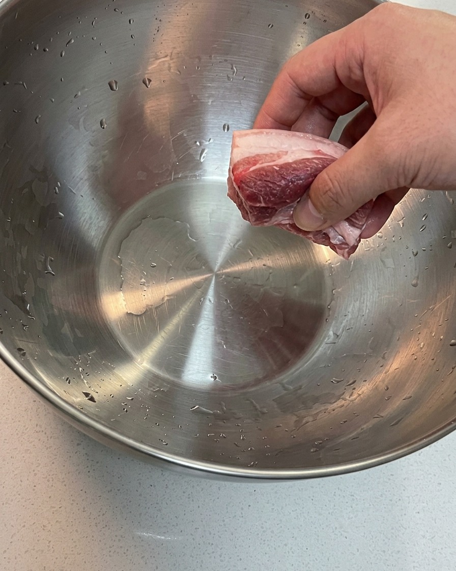 Pork belly and pork shoulder bone soaking in a large bowl of cold water.