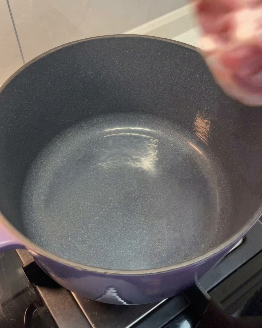 The rinsed pork belly and shoulder bone being placed into a large purple pot.
