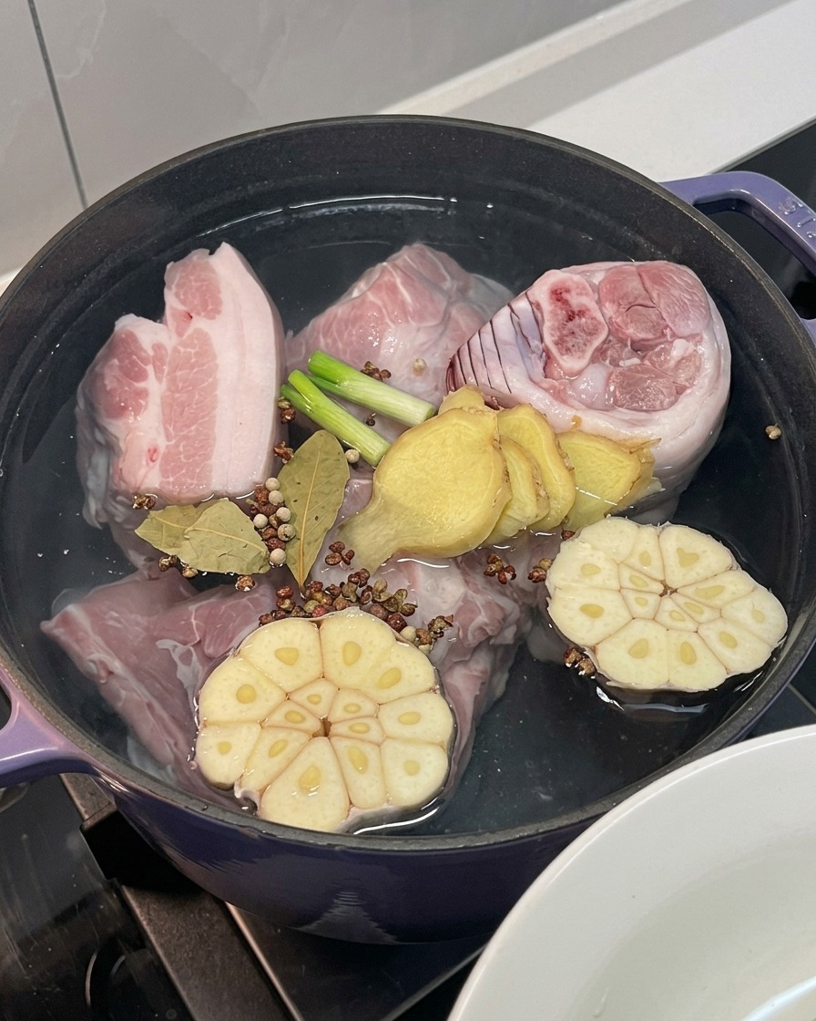 Pork meat in the pot with onion, garlic, ginger, green onion, and whole spices added.