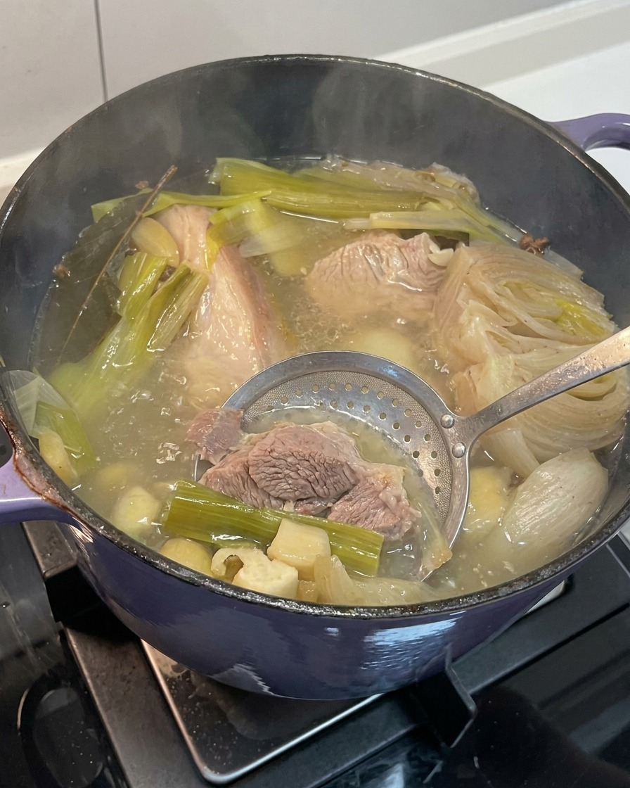 Removing softened onion, garlic, and ginger pieces from the finished pork bone broth.