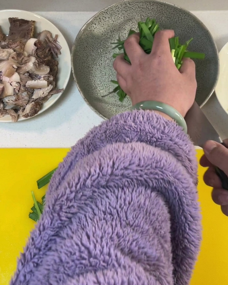 Fresh green chives being cut into segments on a bright yellow cutting board.