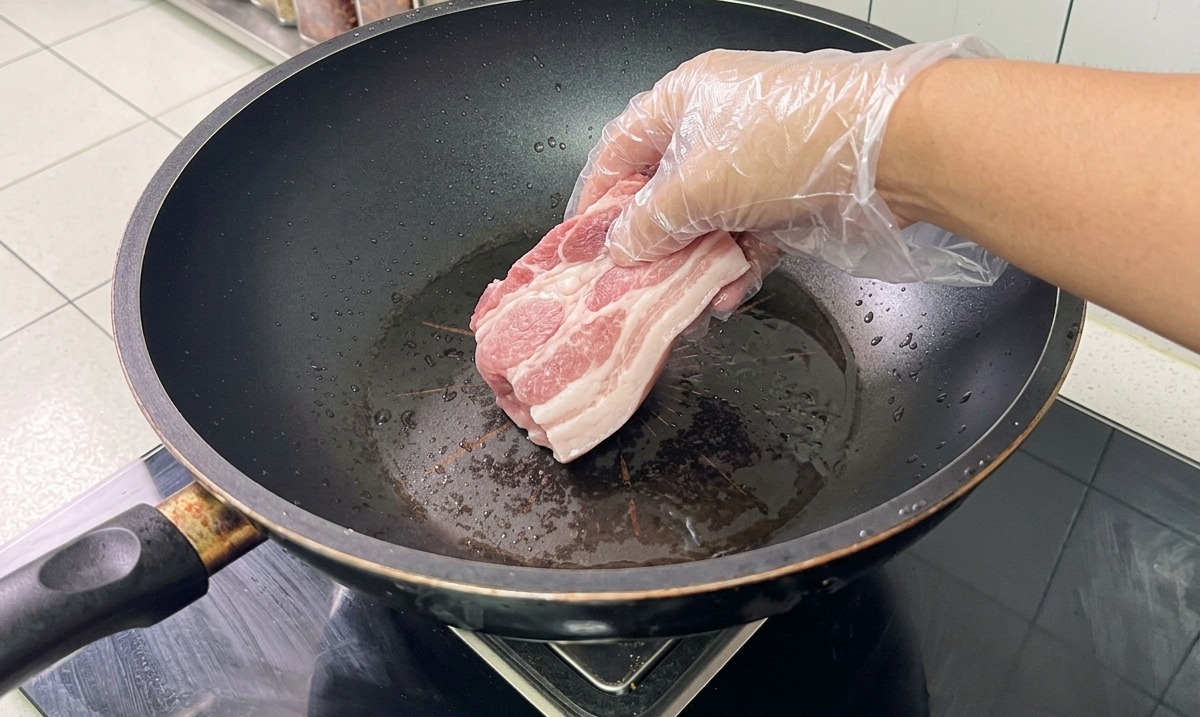 Pork bones and belly in a wok of water with aromatics being blanched.