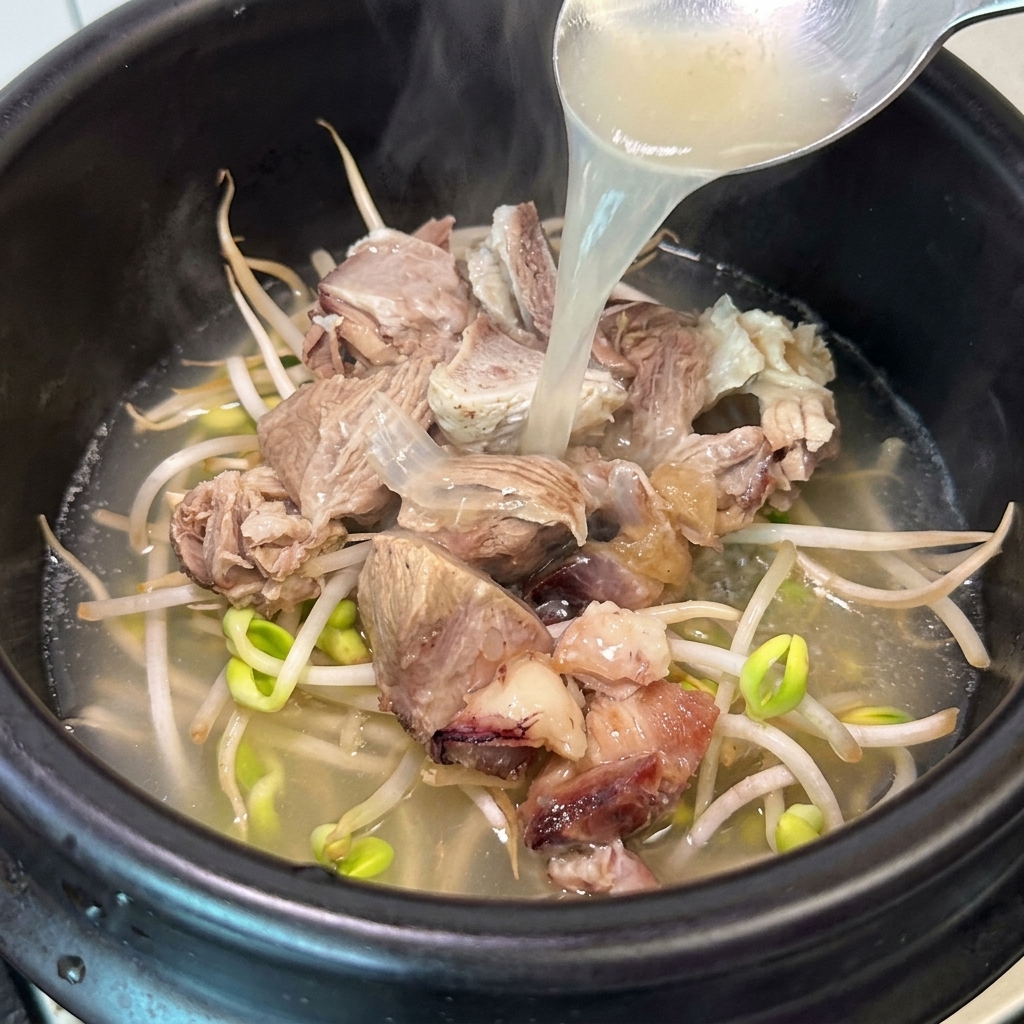A ladle pouring hot, aromatic bone broth into a clay pot containing meat and bean sprouts.