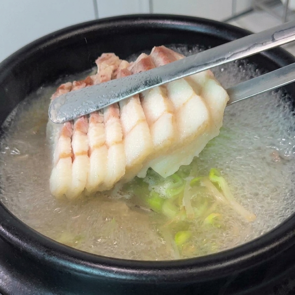 Pork belly slices and chopped chives being added to a boiling clay pot of soup.