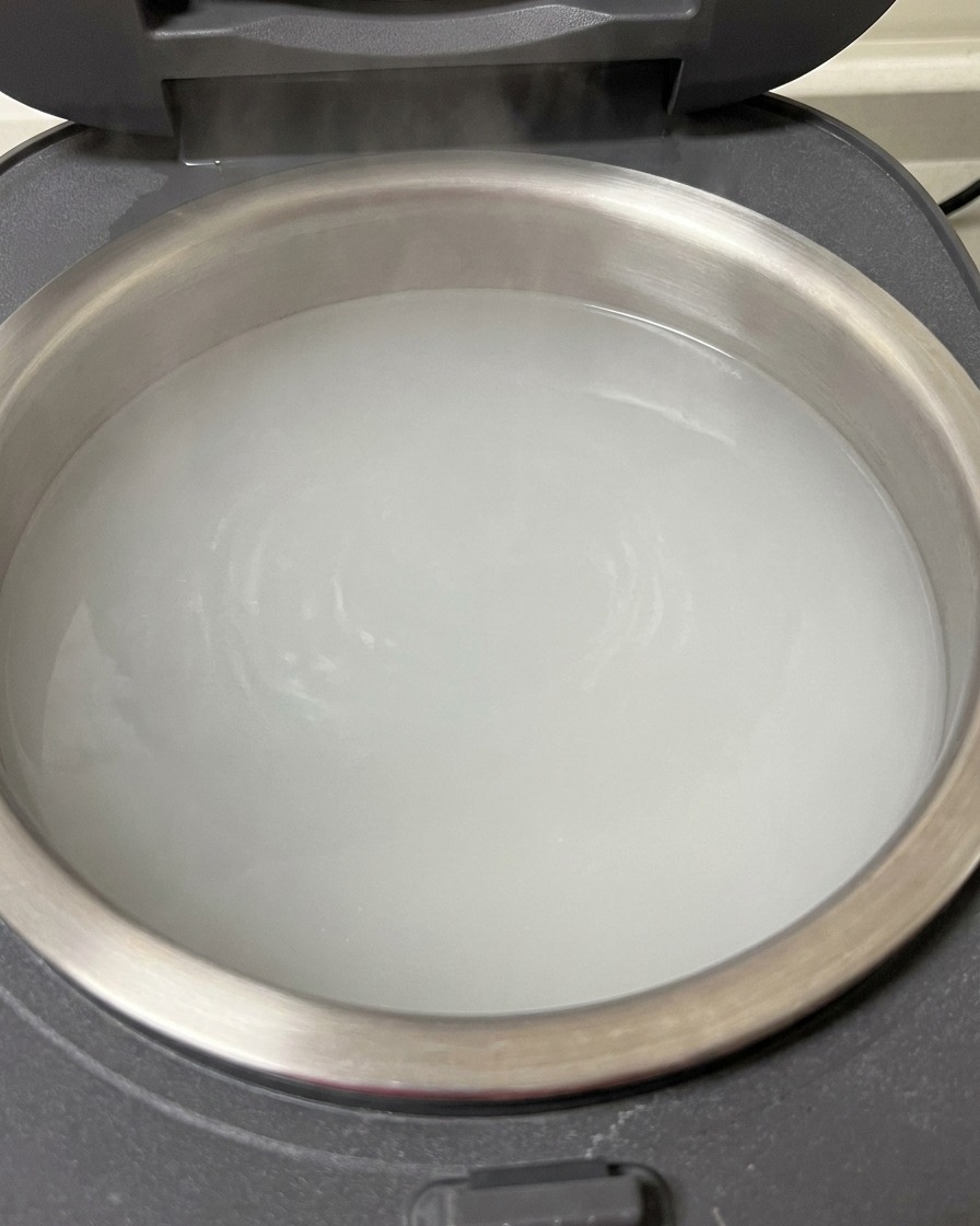 A close-up of raw pork riblets being submerged in a rice cooker pot filled with boiling water.
