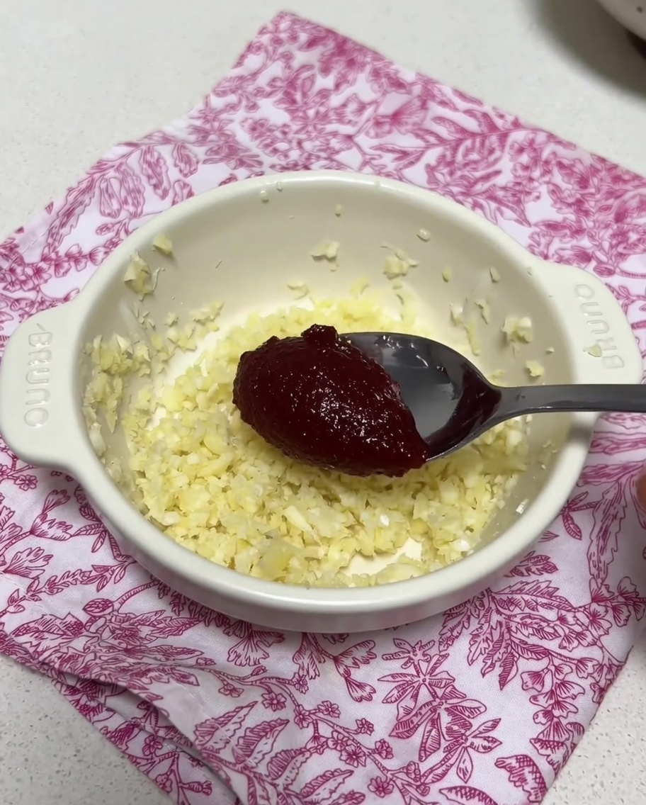 A small bowl containing minced garlic and a dollop of spicy Korean chili paste being mixed with a spoonful of broth.