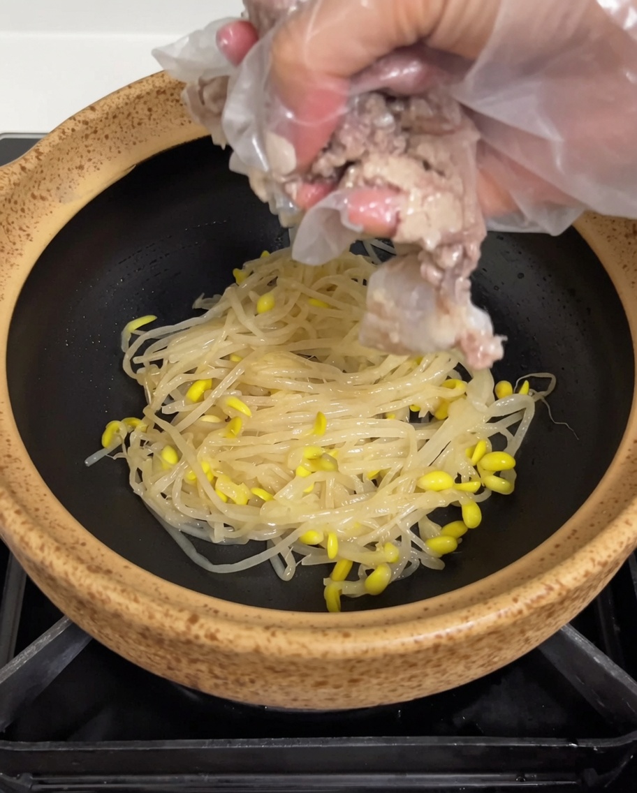 Cooked pork riblets being placed over the bed of soybean sprouts inside the earthen pot.