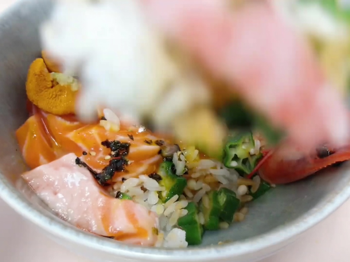 Ingredients being carefully arranged over rice to create the donburi base.