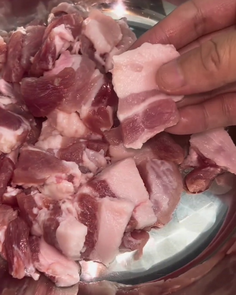 Uniform thin slices of pork belly with visible layers of fat and lean meat arranged in a stainless steel bowl.