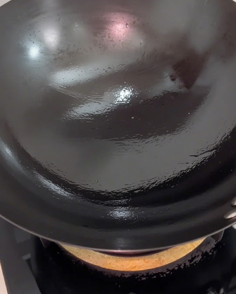 Pork belly slices stir-frying in a wok, showing a light, golden-brown sear on the meat surface.