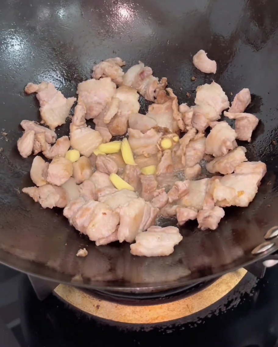 Slices of fresh ginger added to the pork belly in the wok, being stirred together.