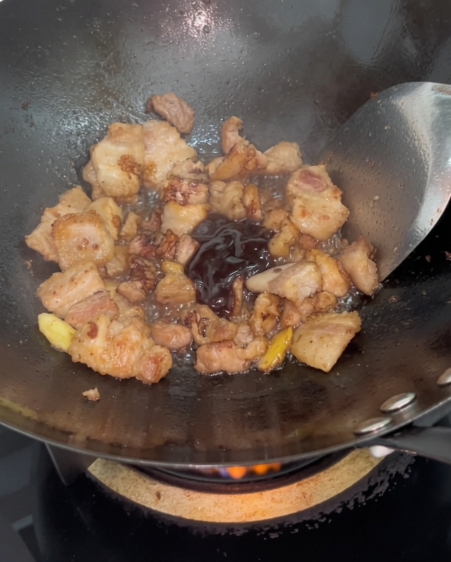 Dark oyster sauce being stirred into browned pork belly slices in a hot wok.