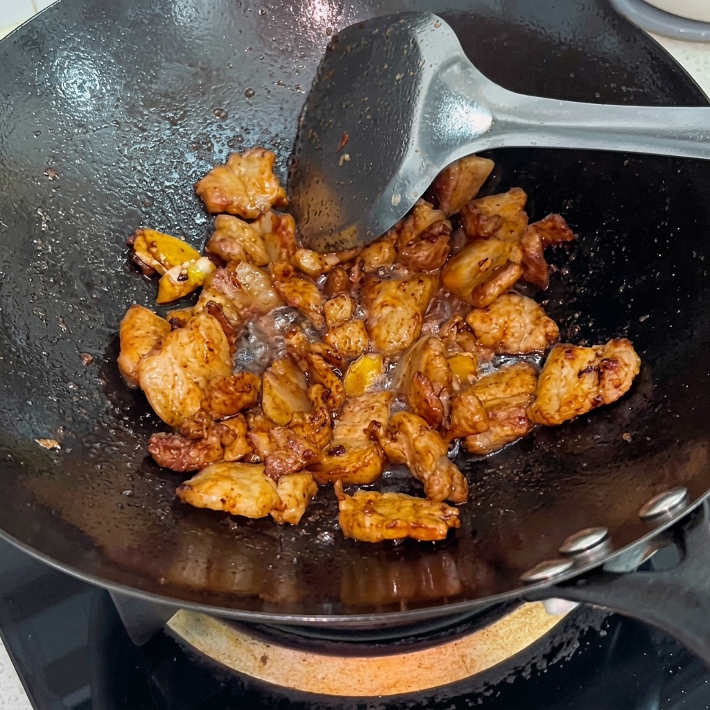 White sugar being sprinkled over glistening, browned pork belly in a wok.