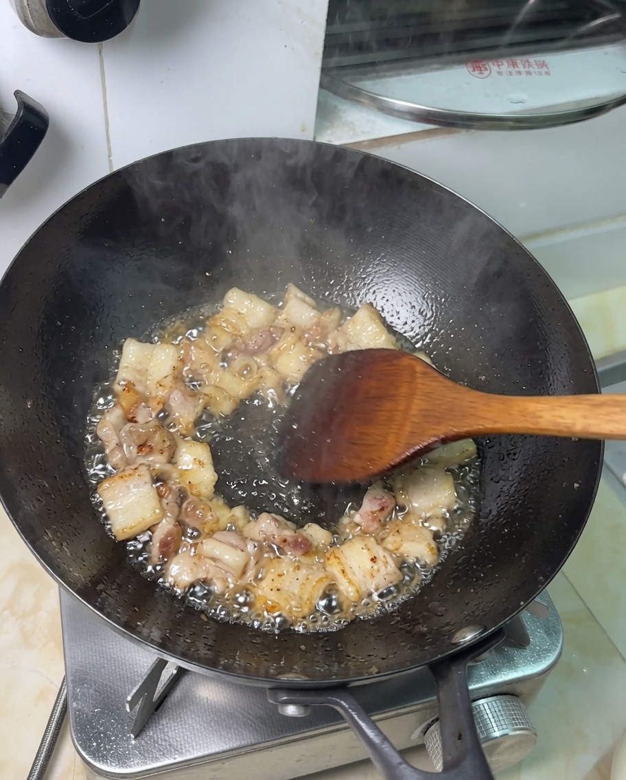 Pork belly pieces frying in rendered fat in a wok.