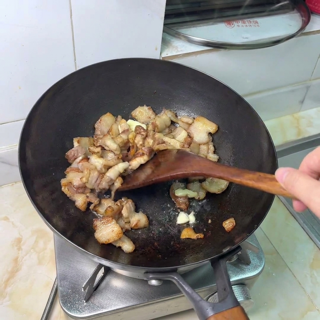 Smashed garlic cloves being stir-fried with browned pork belly pieces.
