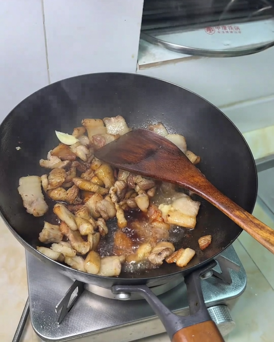 A spoonful of sugar being added to the pork and soy sauce mixture.