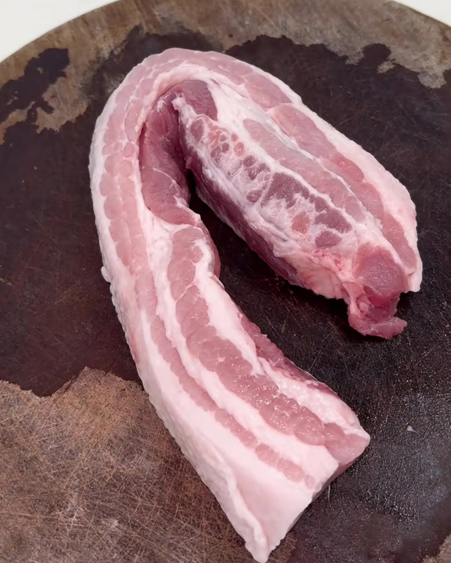 Pork belly slices browning in a hot wok over a stove burner.