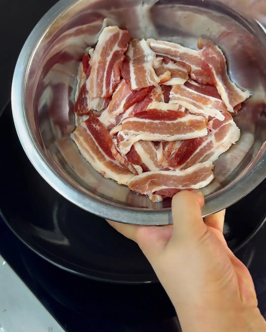 Close-up of pork belly slices being tossed with cornstarch in a metal mixing bowl.