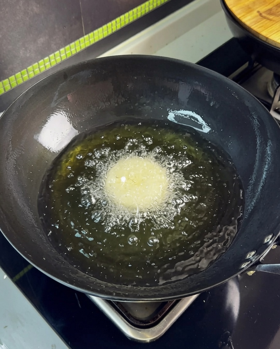 A single pork belly slice being dropped into hot oil in a wok, creating vigorous bubbles.