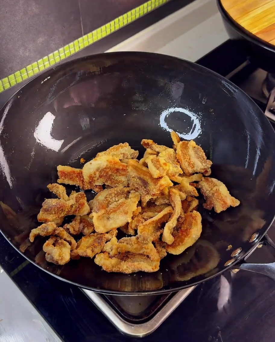 Crispy fried pork belly pieces in a wok being stir-fried with garlic and soy-based sauce.
