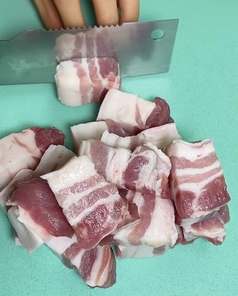 Raw pork belly pieces in a pan filled with cold water, ginger, and cooking wine.