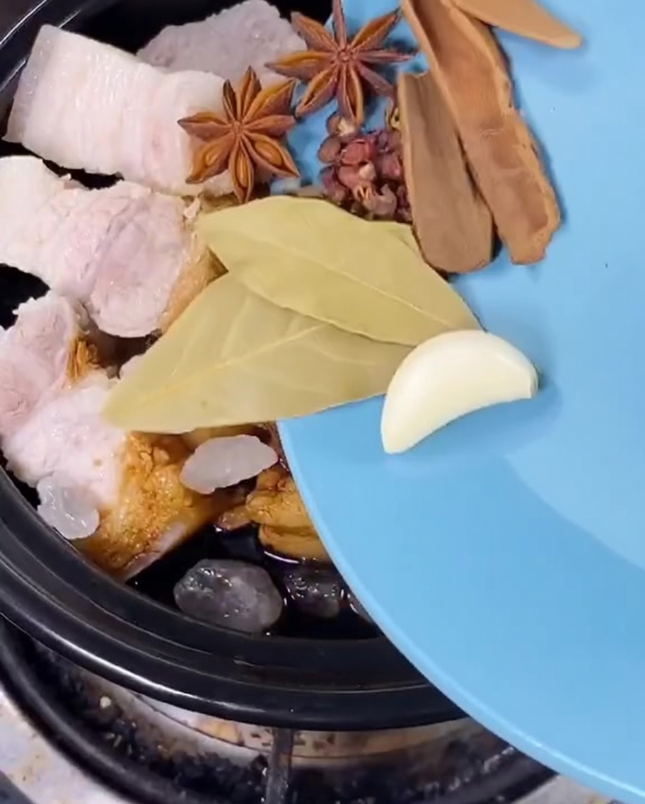 Star anise, bay leaves, dried citrus peel, and green onions being added to the pot of pork.