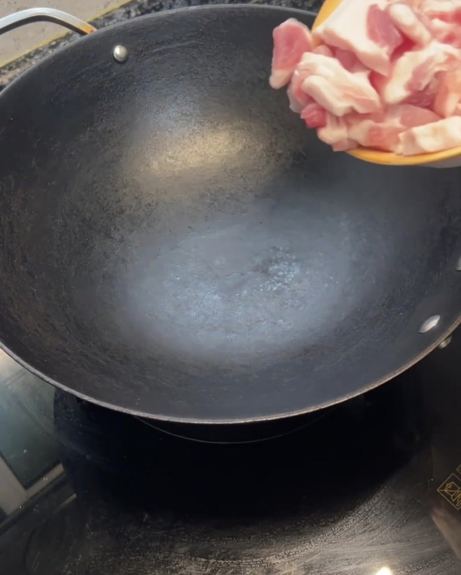 Slices of raw pork belly being dropped into a hot, empty wok.