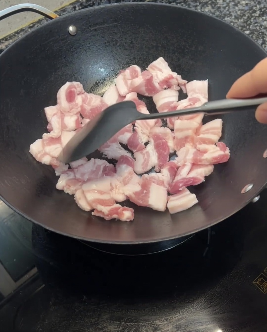 Pork belly slices being stir-fried in a wok with a spatula, showing signs of browning.