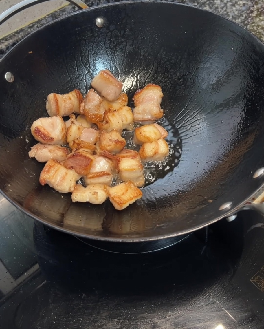 Garlic cloves being added to the wok with the browned pork belly.