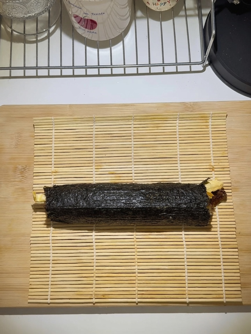 A tightly rolled gimbap on a bamboo rolling mat.