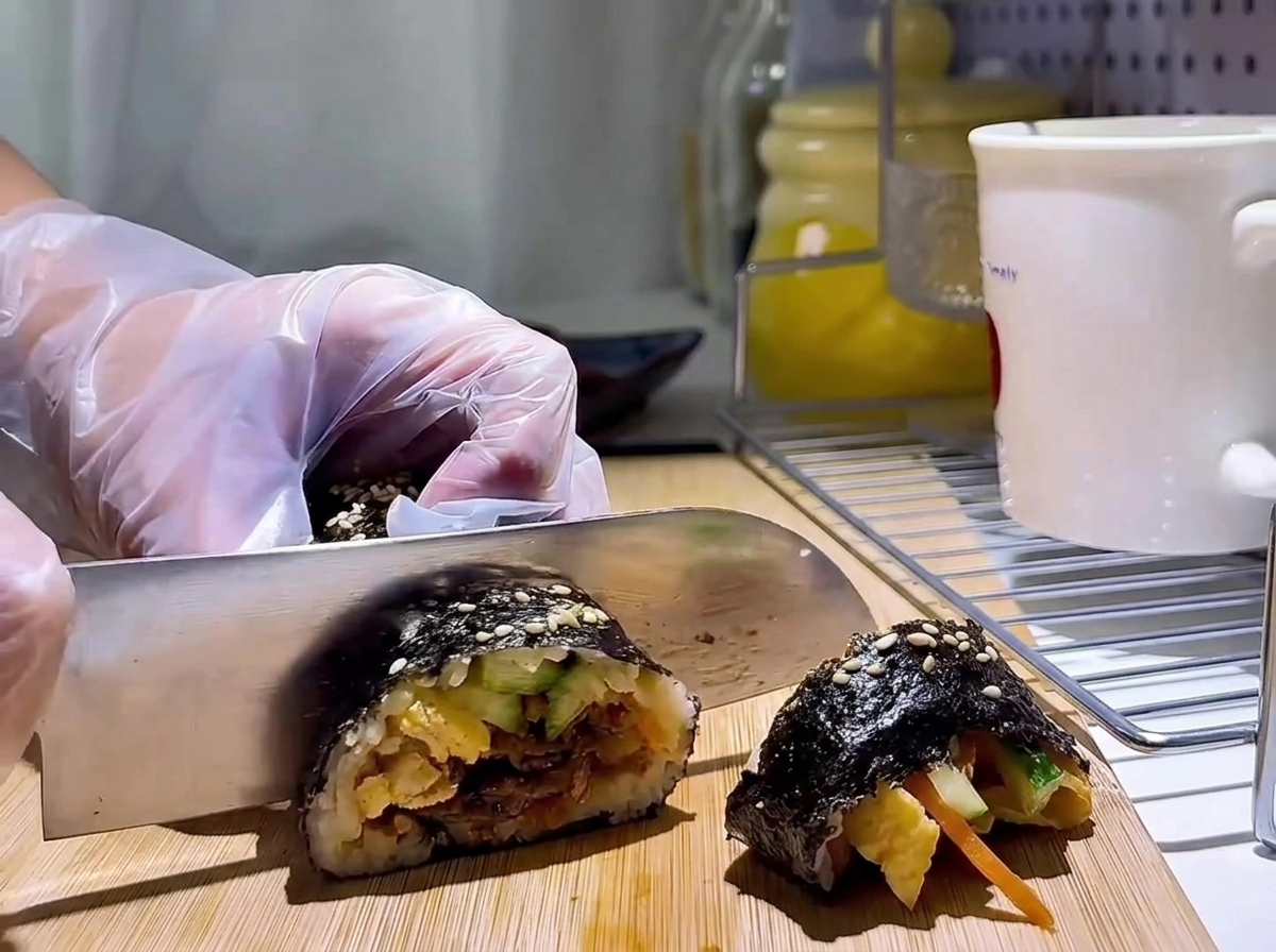 A sharp knife slicing the seaweed roll into round pieces on a wooden cutting board.