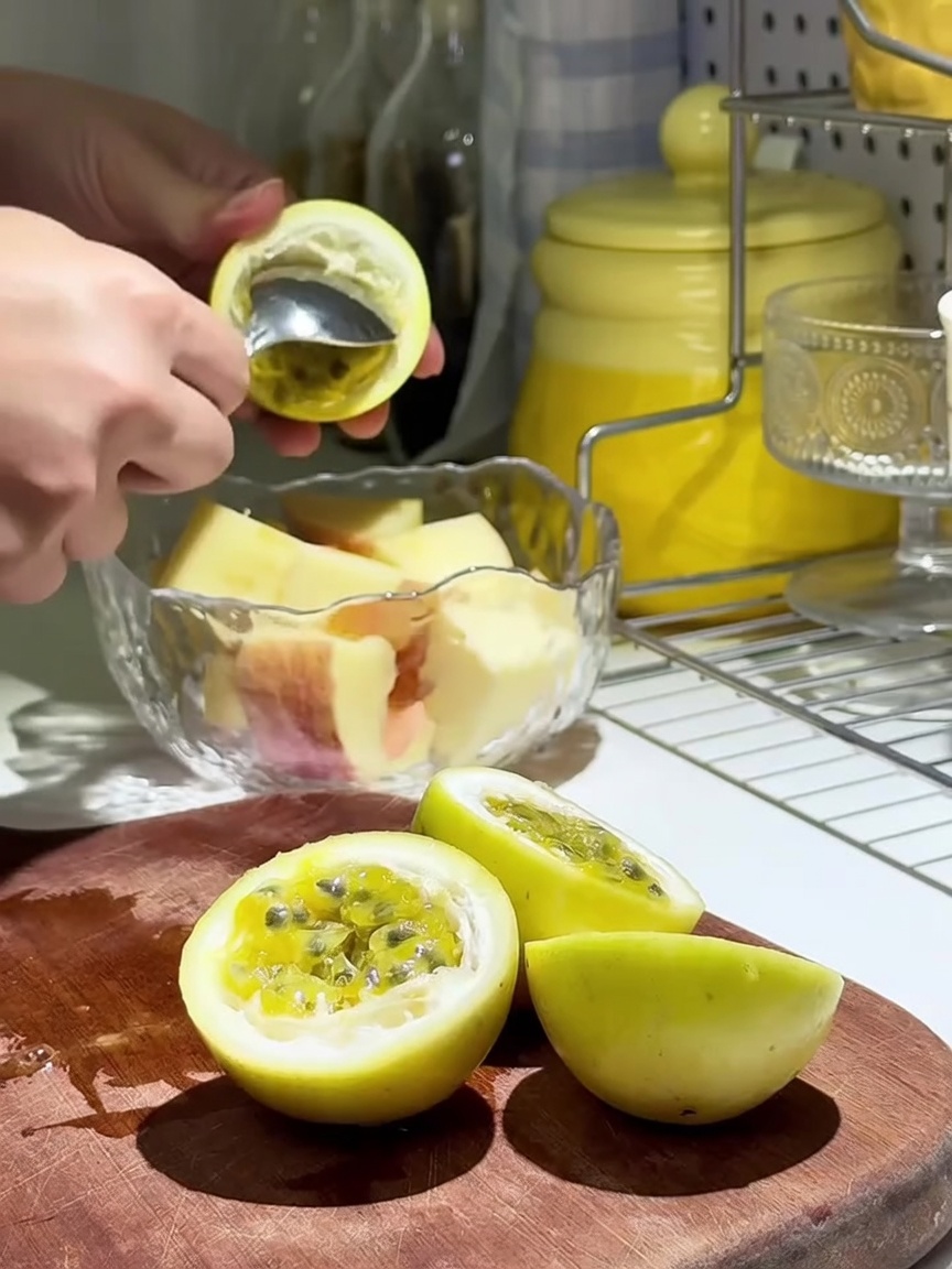 Fresh passion fruit pulp being scooped over apple slices in a glass bowl.