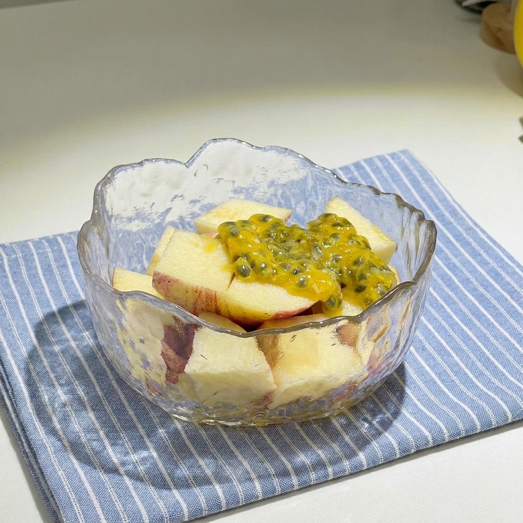 A glass bowl filled with diced red apples topped with yellow passion fruit pulp and drizzled with honey.