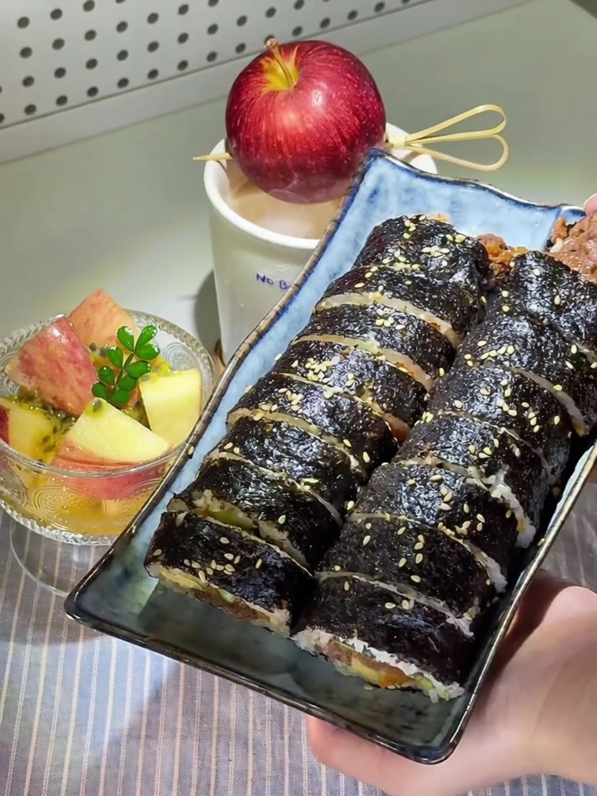 Sliced Korean beef gimbap garnished with sesame seeds, accompanied by a crystal bowl of passion fruit pickled apples.