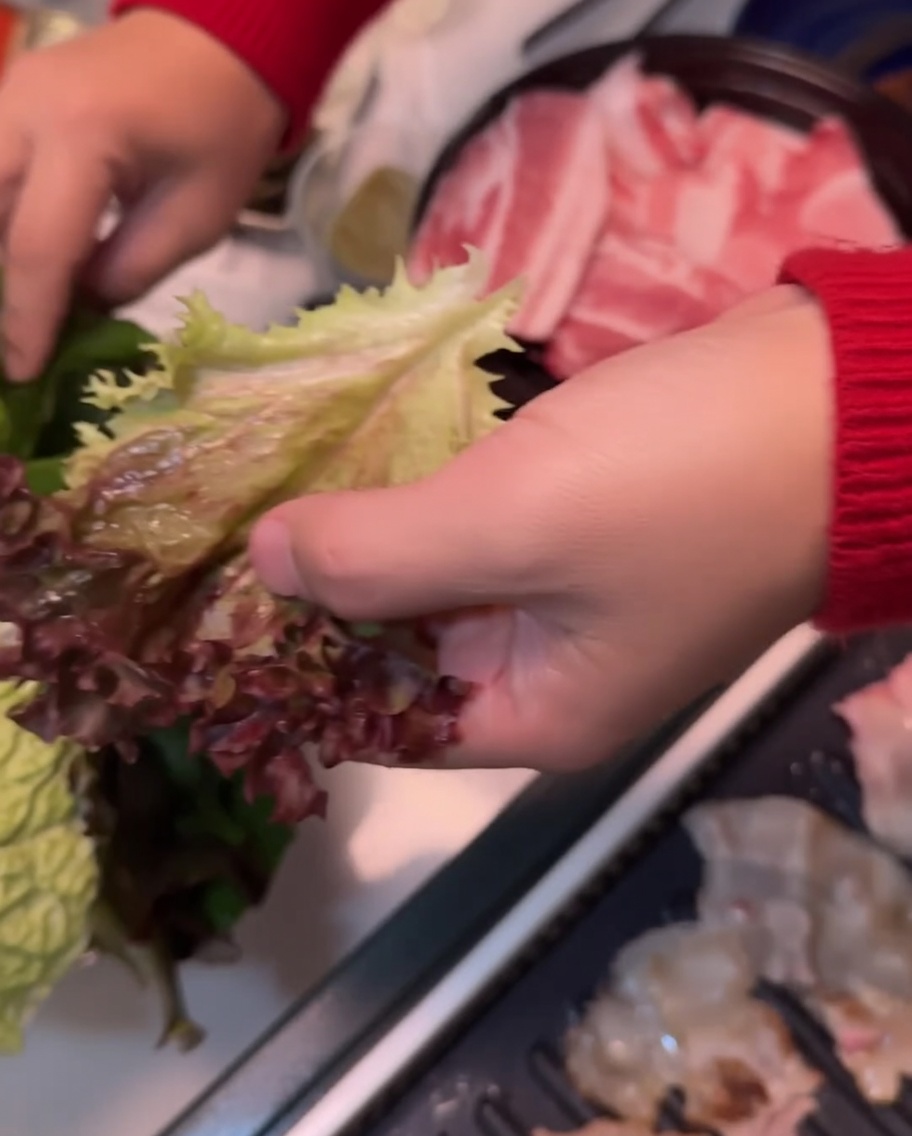 A lettuce leaf being placed over a perilla leaf in a hand, ready for assembly.