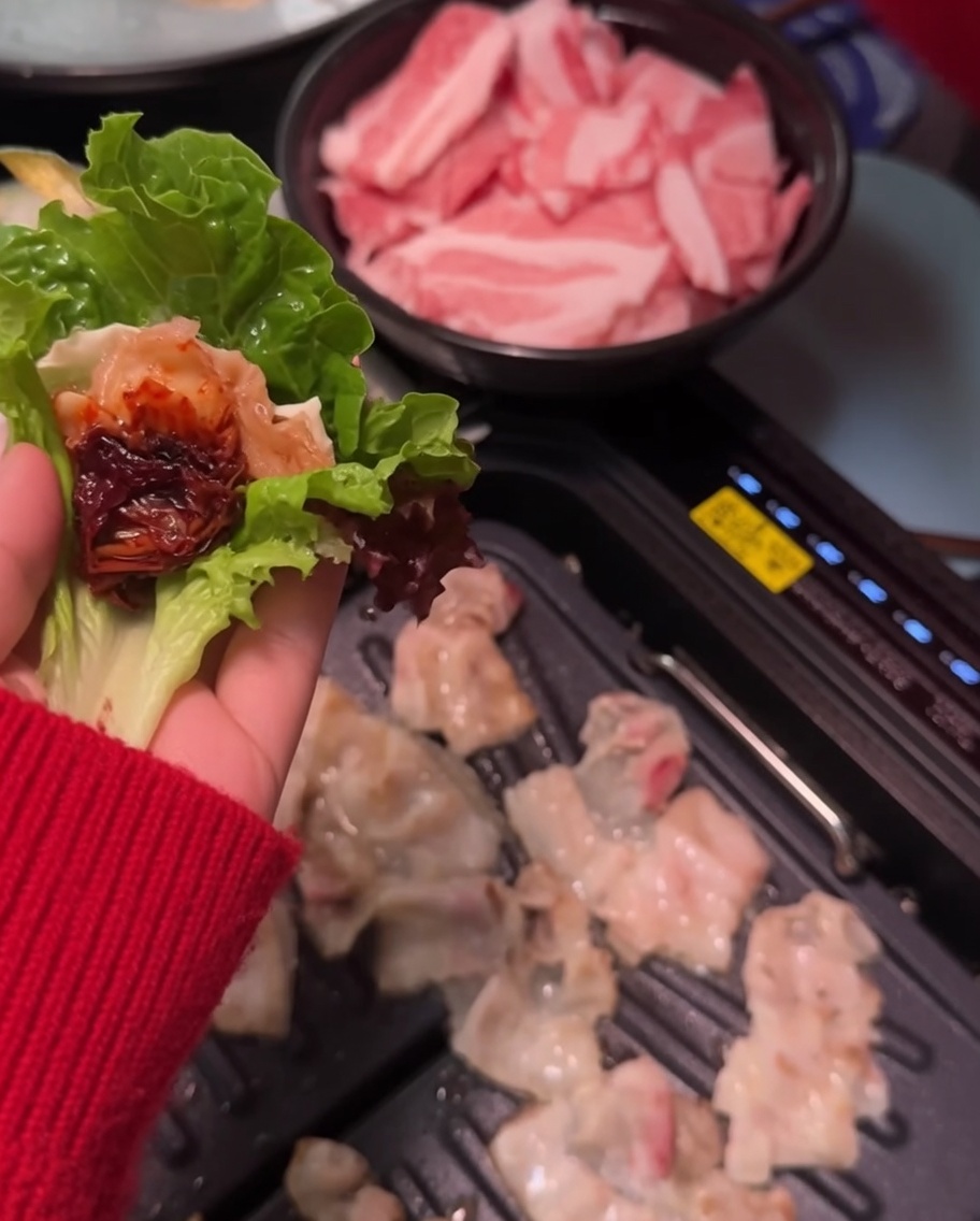 Spicy soybean paste being applied onto a slice of pork belly on a leaf.