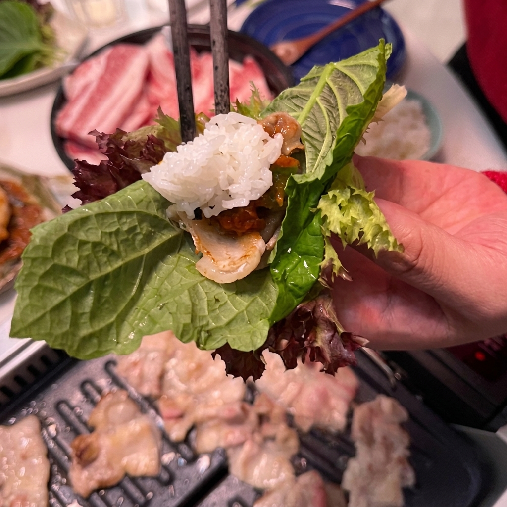 A spoonful of white rice being added to a lettuce wrap containing pork and sauce.