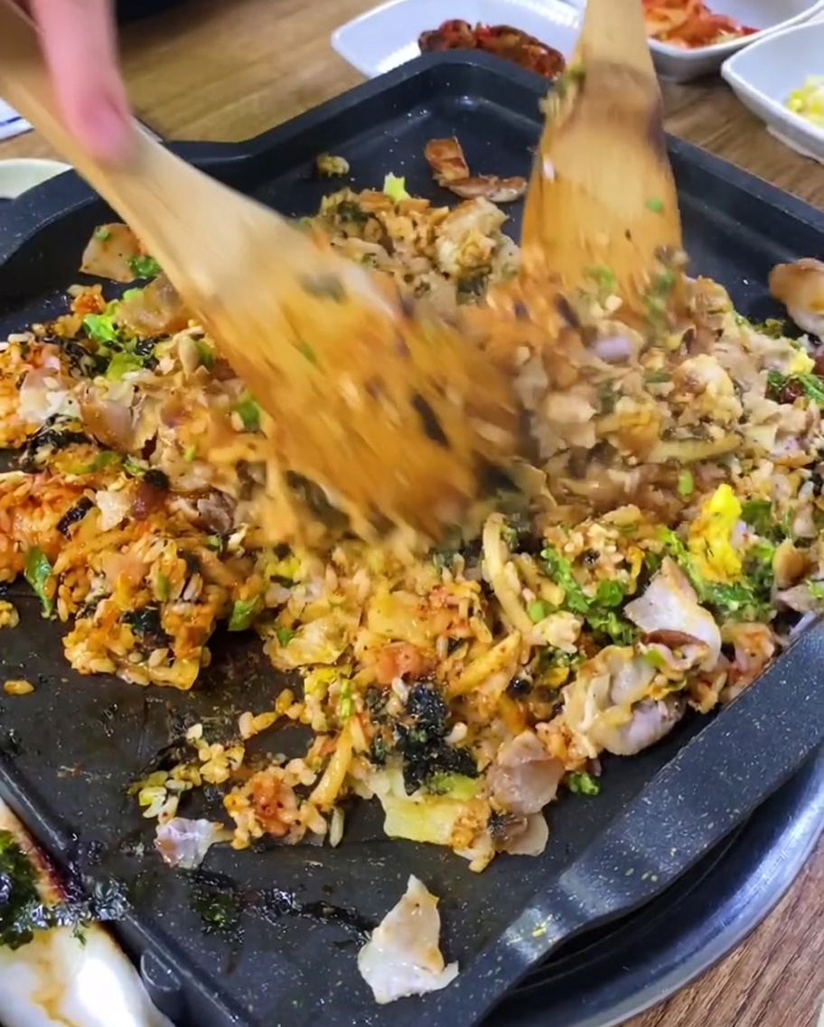 Fried rice being stir-fried with pork pieces on a hot griddle.