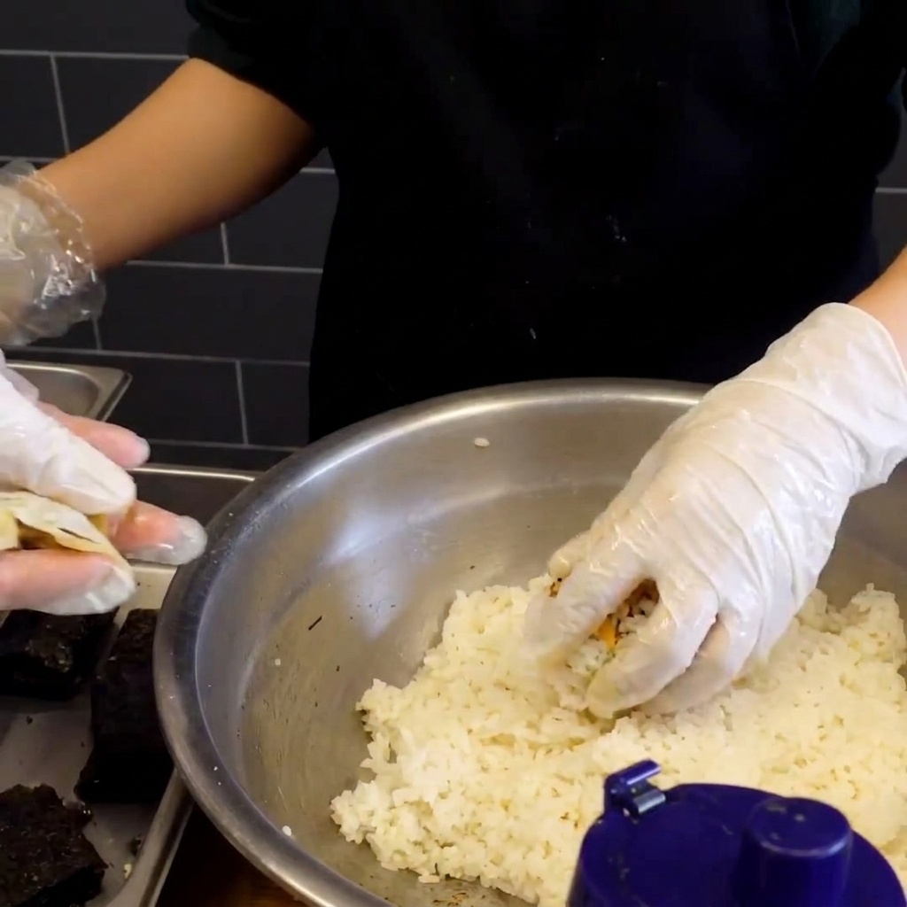 A freshly shaped sticky rice ball with a small square of dark, dried seaweed pressed onto its surface.