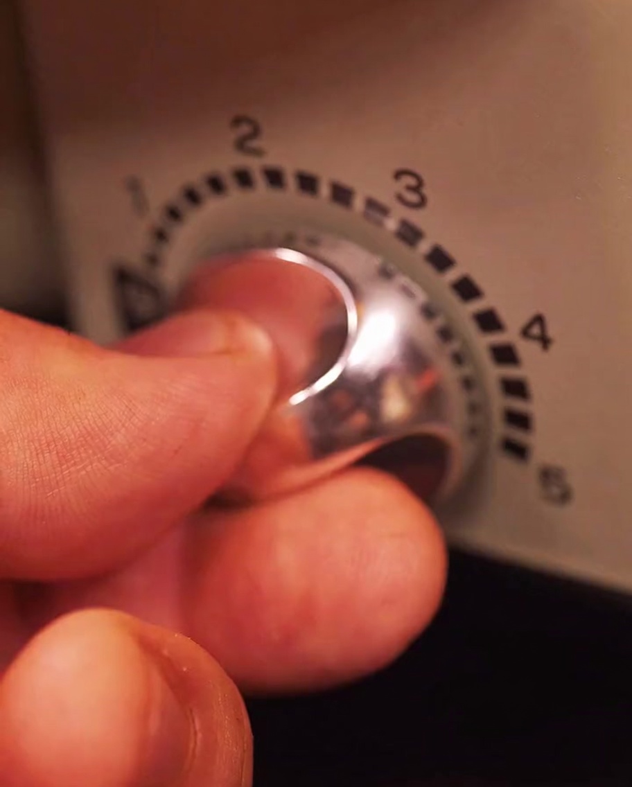 Hand adjusting the heat dial on an electric grill to increase intensity.