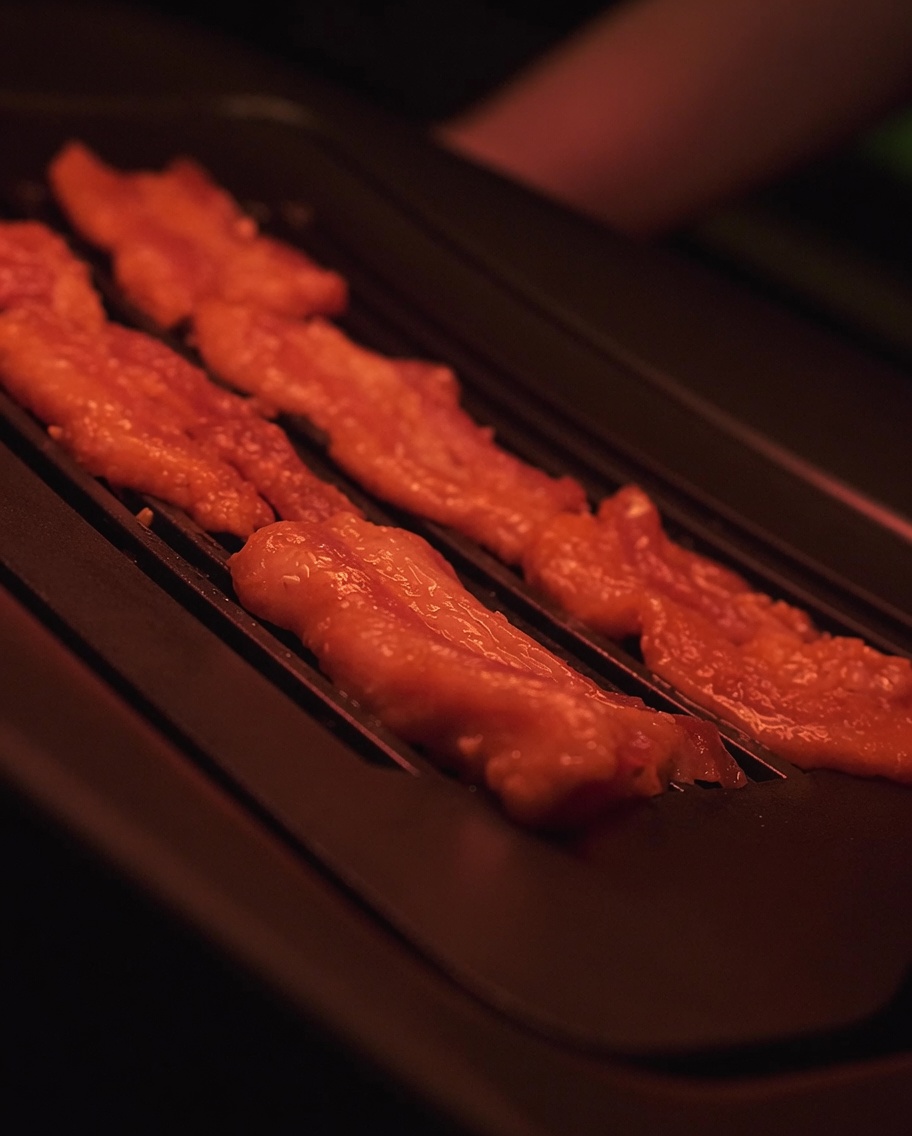 Marinated pork belly slices sizzling on a hot electric grill surface.