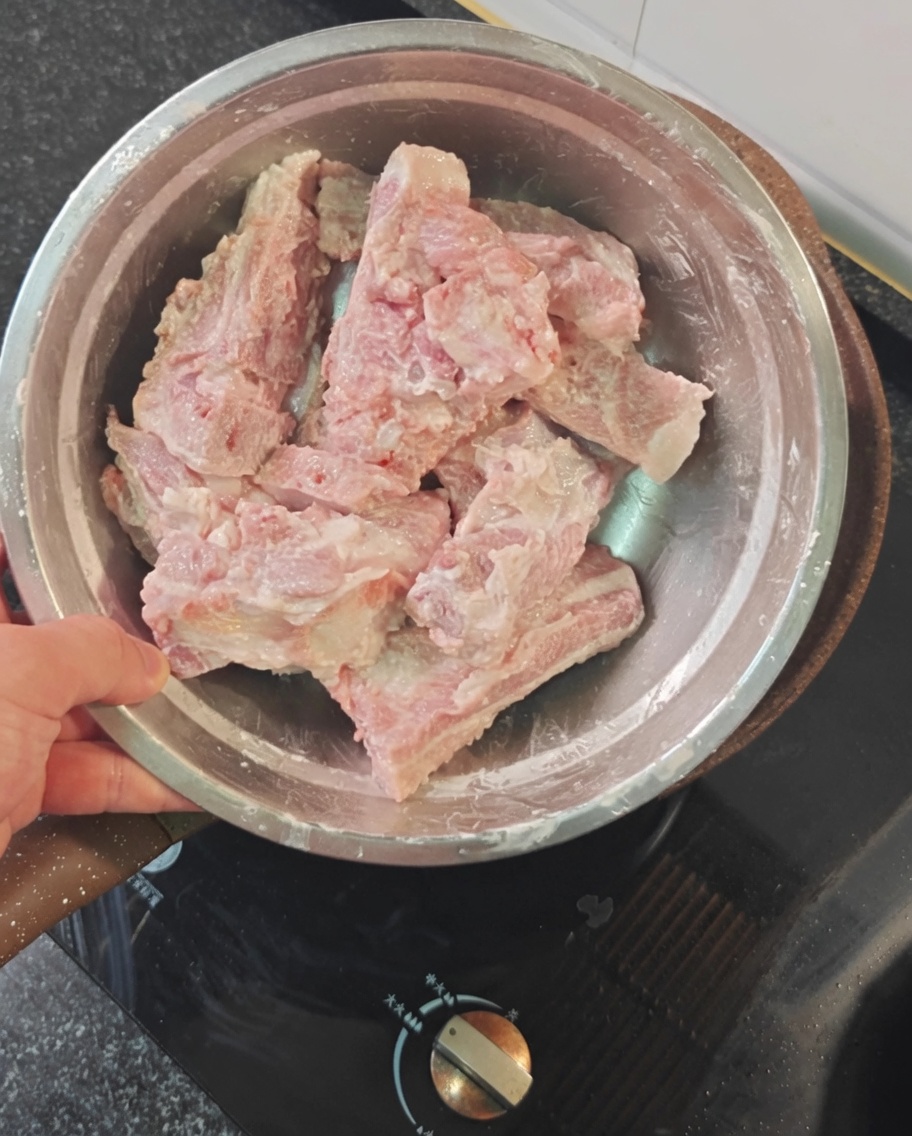 Raw pork ribs coated in red starch powder inside a metal bowl.
