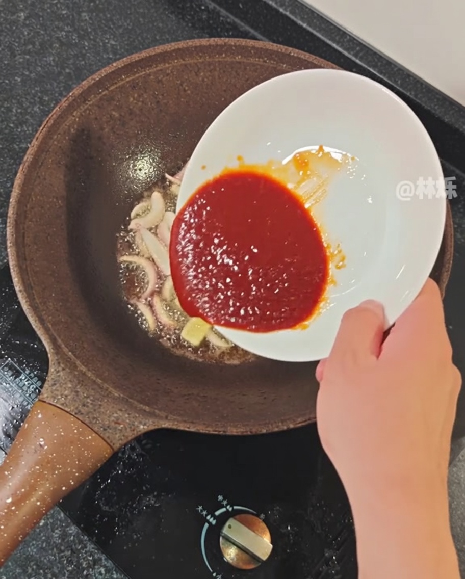 Spicy sauce being poured into a pan with sautéed aromatics.
